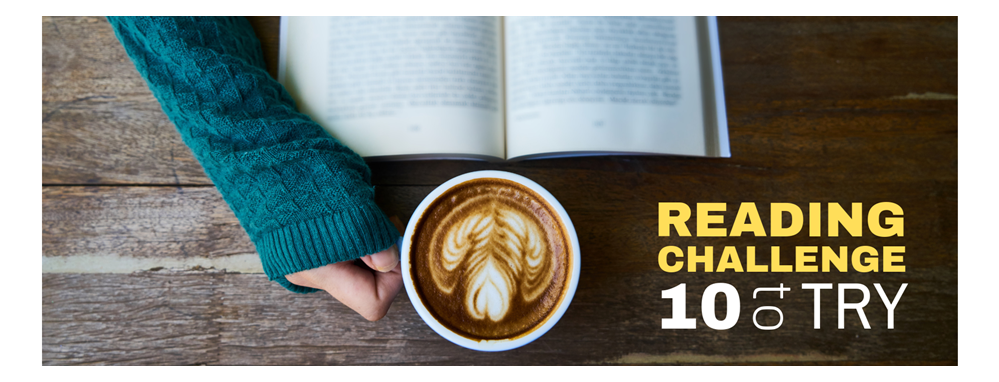 a bird eye view of a feminine hand holding a fancy cup of coffee with a open book infront, implying she's reading when really she's enjoying that 15 dollar coffee